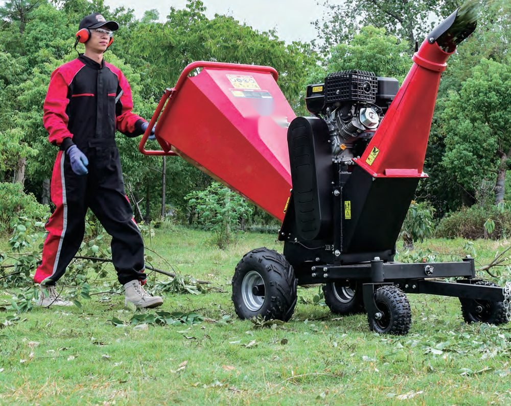 Operator feeding branches into a towable petrol wood chipper